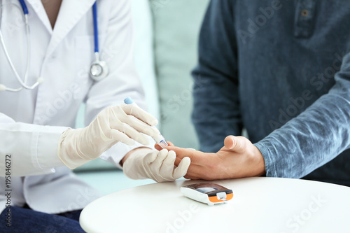 Doctor taking sample of diabetic patient's blood using lancet pen, closeup photo