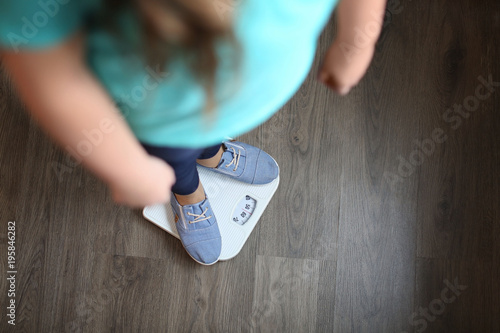 Overweight girl standing on floor scales indoors photo