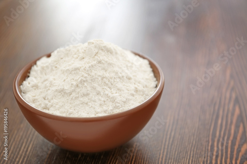 Bowl with wheat flour on wooden background