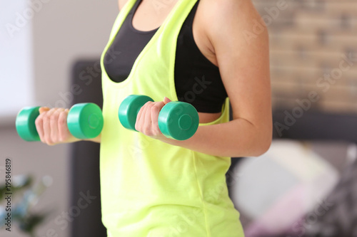 Beautiful young woman doing fitness exercise with dumbbells at home