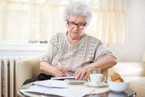 Old woman calculating bills at home.