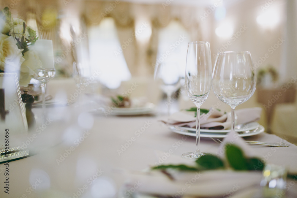 Beautiful decoration of a wedding banquet in a restaurant in pastel colors. Serving the table with beige tablecloth, plates, glasses, cutlery, napkins decoration with a green twig