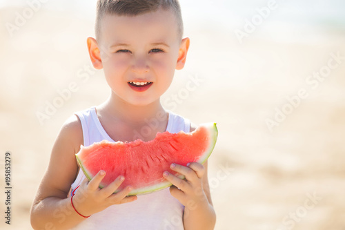 Adorable kid at the sea shore eating juicy watermelon. Cheerful child on summer time on the beach. Cute little boy outdoors