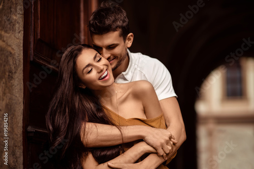Happy young female with long dark hair glad to recieve passionate kiss from her boyfriend. Handsome male embraces his girlfriend and kisses. Portrait of lovely young couple express mutual love.