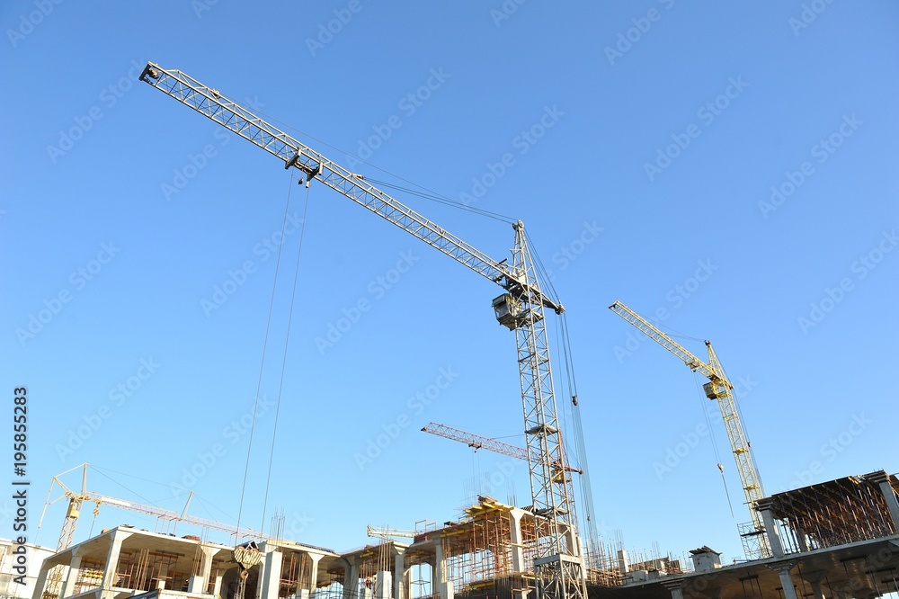 Construction cranes on the construction of a large house on a blue sky background