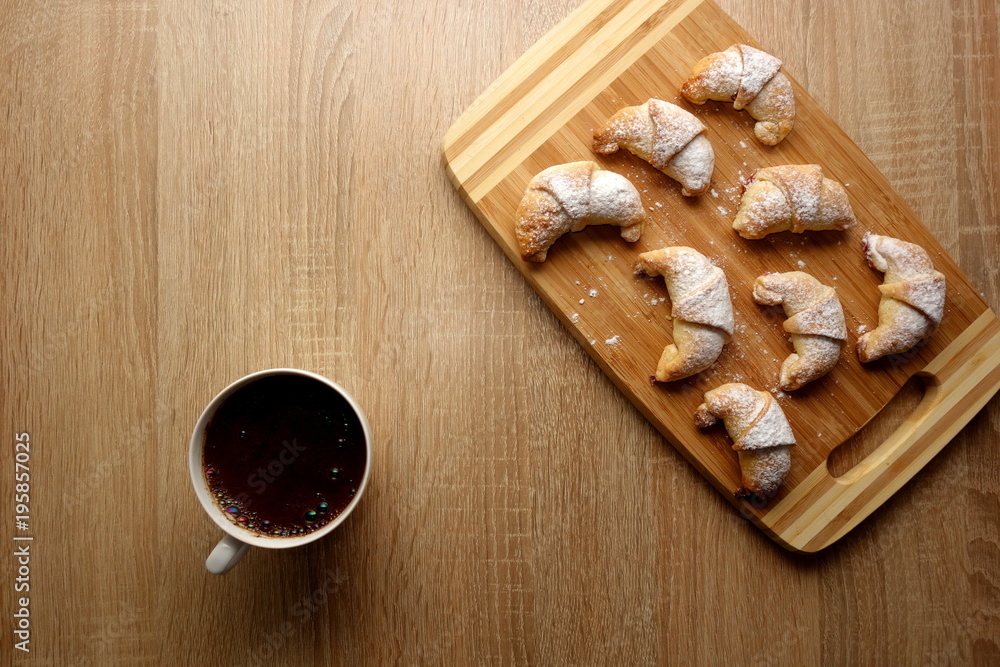 Cup of fresh black coffee with homemade croissants on rustic wooden table background, view from above, copy space for a text