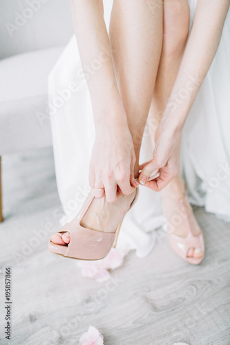 Young woman puts on pink high heel shoes in bright room with rose flower buds. Wedding bridal fashion concept. © Floral Deco