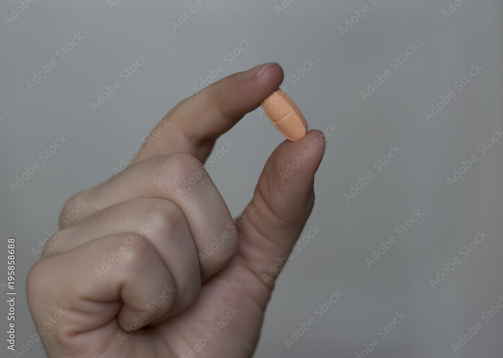 A pill in a woman's hand against a gray background. Close-up. The concept of medicine. A pill in a woman's hand against a gray background. Close-up. The concept of medicine.
