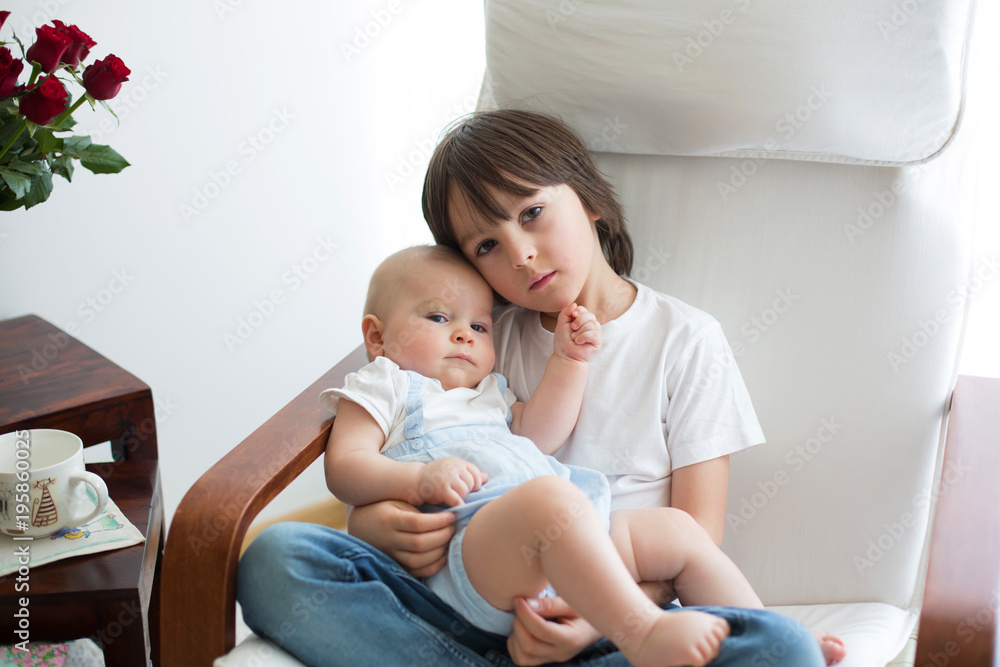 Adorable preschool child, hugging his baby brother in rocking chair Adorable preschool child, hugging his baby brother in rocking chair
