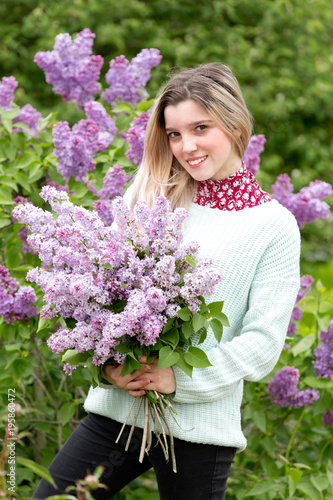 Beautiful young girl with a bouquet of lilacs in the garden
