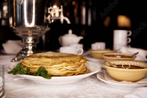 On the serving table is a white plate with thin fried pancakes decorated with mint sprigs and a clay dish with jam.