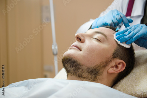 Doctor aesthetician makes beauty injections in forehead of male patient