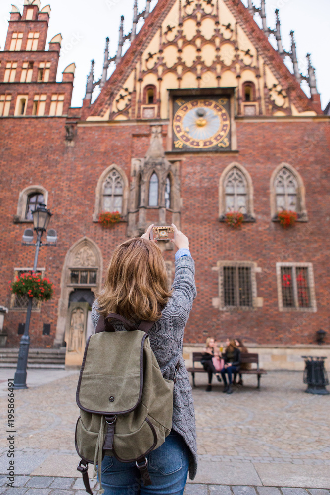A woman traveler takes pictures of a landmark by phone camera.
