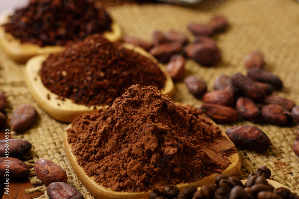 Cacao powder, cocoa nibs, and coffee beans on wooden plates on burlap