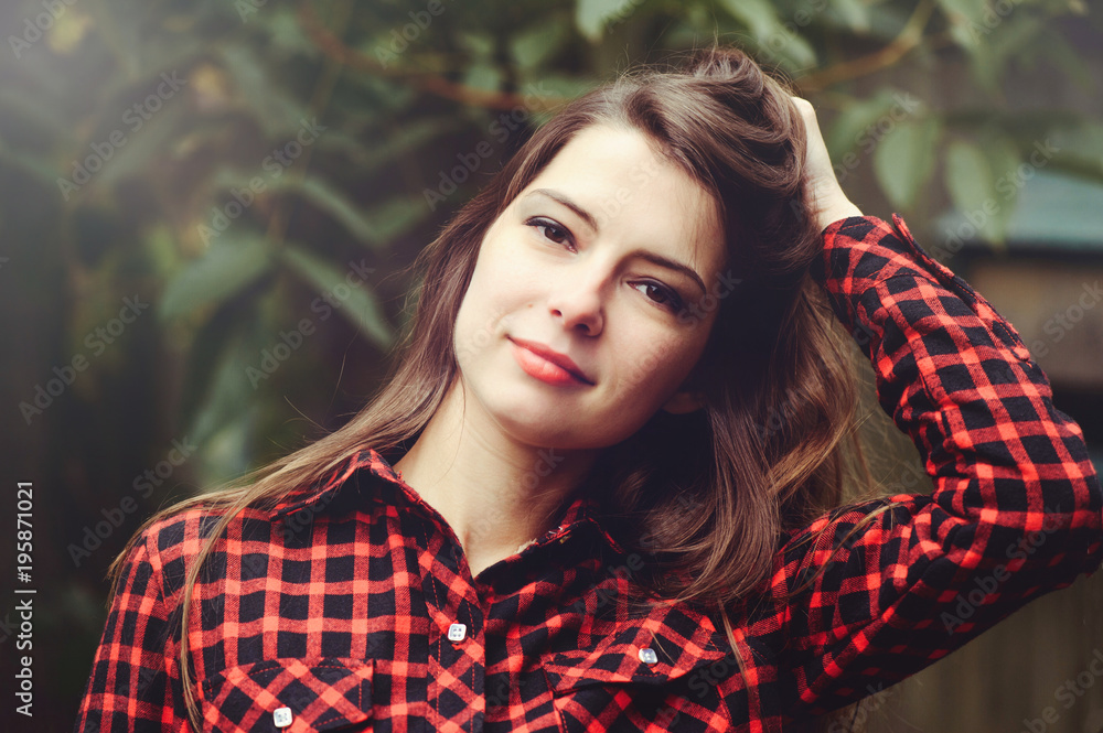 Smiling young brunette woman posing in the courtyard of her residence in a red checkered shirt is happy, portrait of happy carefree, health