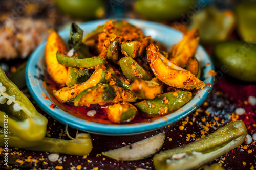 Close up of Aam ka achar or kari ka achar with all its ingredients and speiceis on a wooden surface in drak Gothic colors.