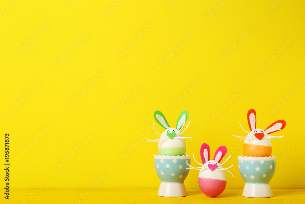 Eggs with funny rabbit faces on yellow background