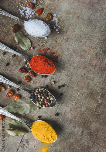 Close up and top view of vintage spoons filled with colorful spices, curcuma or turmeric, allspice pepper, red pepper and salt on old rustic wooden background with space. Vintage toned. 