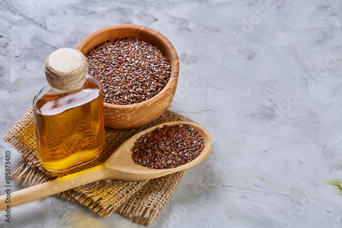 Flax seeds in bowl and flaxseed oil in glass bottle on light textured background, top view, close-up, selective focus