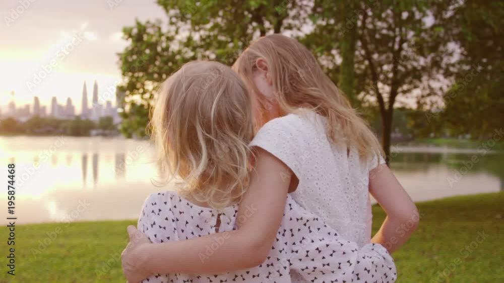 Two sisters admire the sunset in the city park by the lake. Slow motion. Two sisters admire the sunset in the city park by the lake. Slow motion.