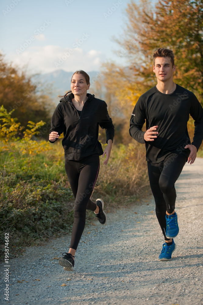 Young veautiful couple runs on a path in park on autumn afternoon Young veautiful couple runs on a path in park on autumn afternoon
