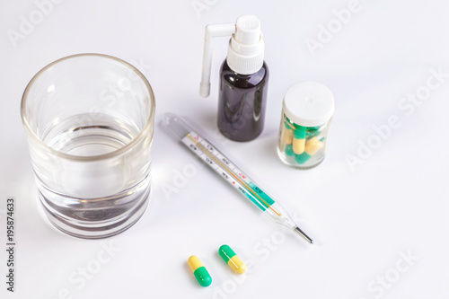 Tablets, a glass of pure water, a thermometer. On a white background.