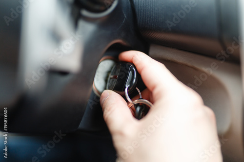 The driver of the man gets a car with a key. The hand inserts the key into the ignition and starts the car. Hand put the car key to the keyhole starting the car.