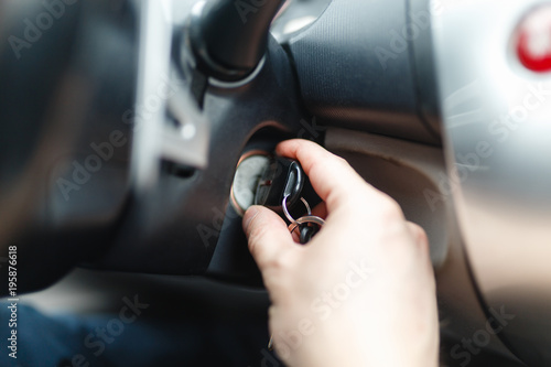 The driver of the man gets a car with a key. The hand inserts the key into the ignition and starts the car. Hand put the car key to the keyhole starting the car.