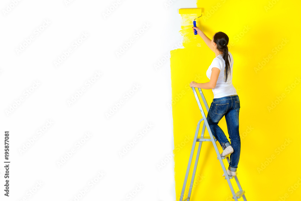 girl painter paints a wall with a platen standing on a staircase