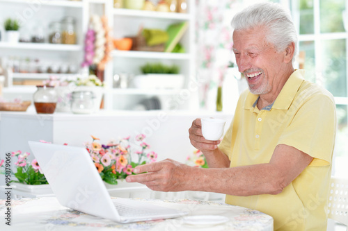 happy senior man using  laptop while drinking tea