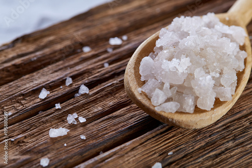 Crystal sea salt in a wooden spoon on dark vintage wooden background, top view, close-up, selective focus.
