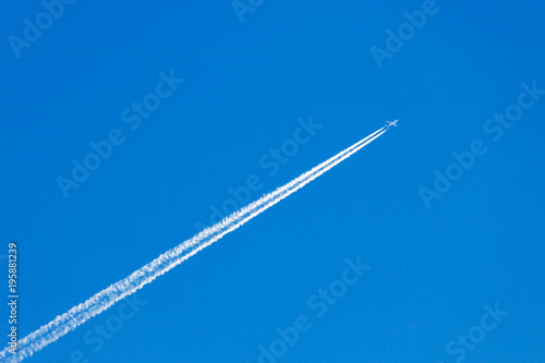 Modern jet plane with white condensation track flies on a blue sky background