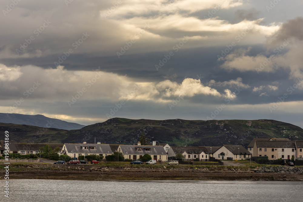 Aultbea, Scotland - June 8, 2012: Calm waters of Loch Ewe with the community of Aultbea under dark rainy cloudscape. Dark hills in background.