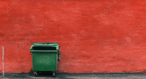 green garbage container on a red wall background