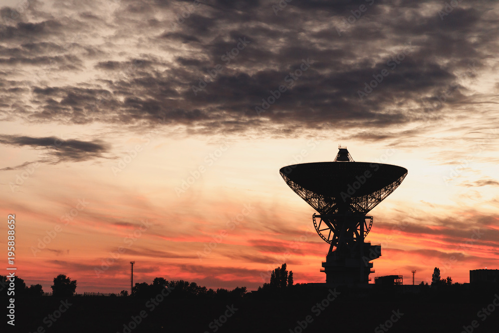 huge white radio telescope of a satellite dish against the sky during sunset