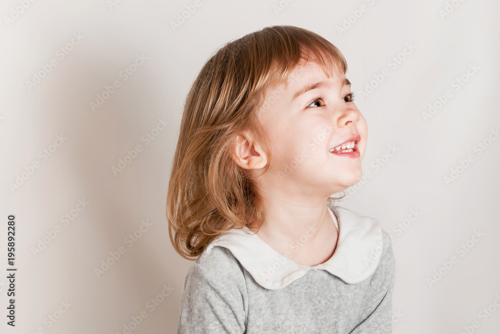 Little girl stand on the light background, looks aside and smiles. Little girl stand on the light background, looks aside and smiles.