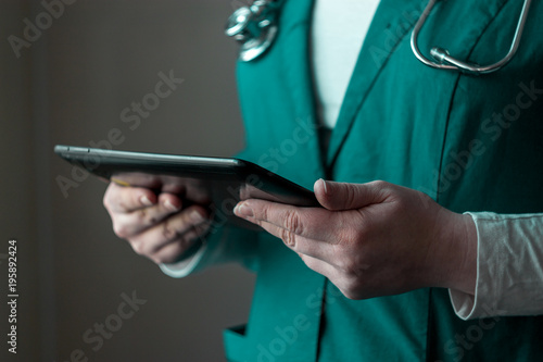 doctor in green uniform stands at half a turn and holds a tablet