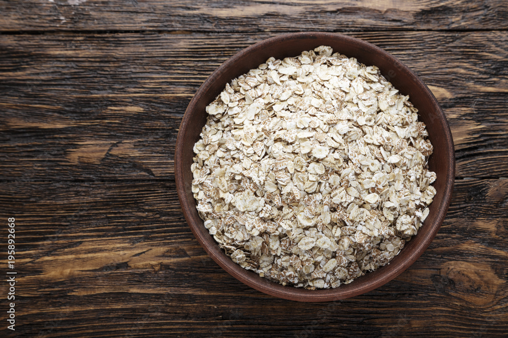 raw oatmeal in a bowl, on a brown wooden table. raw oatmeal in a bowl, on a brown wooden table.