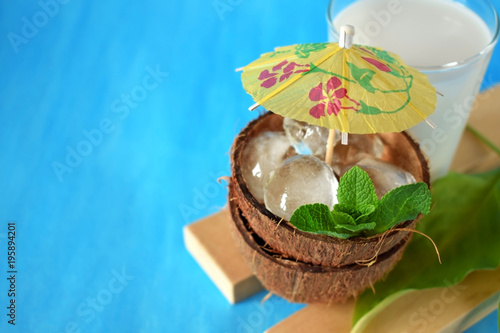 Coconut halves with ice cubes. A glass of coconut milk next to it. Ingredients for a tropical cocktail on blue background