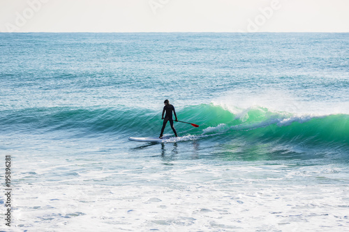 Surfer on stand up paddle board on ocean waves. Stand up paddle boarding in sea © artifirsov