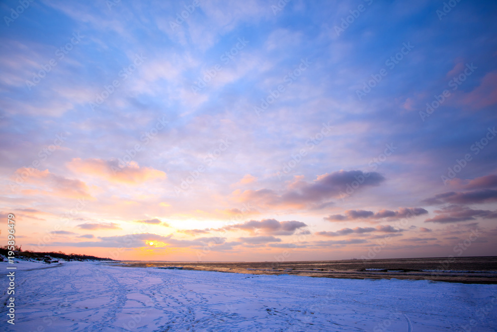 a beach under snow and a cold, ice-covered sea during sunset