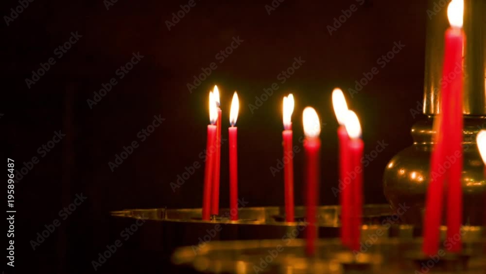 A person places a red wax candle lit in an Asian temple. There are several red candles with flame. A person places a red wax candle lit in an Asian temple. There are several red candles with flame.