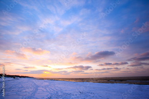 a beach under snow and a cold  ice-covered sea during sunset