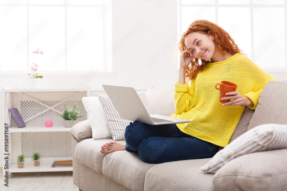 Fototapeta premium Enjoying free time at home. Smiling girl with laptop on sofa