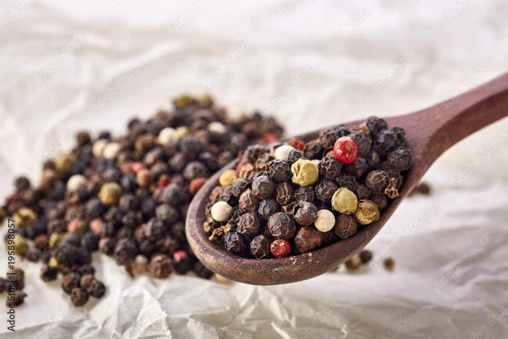 Composition of peppercorns in wooden spoon on white background, close-up, shallow depth of field Composition of peppercorns in wooden spoon on white background, close-up, shallow depth of field