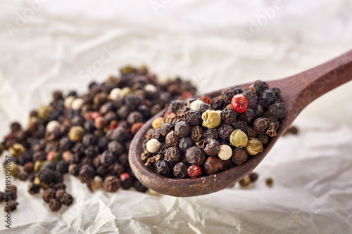 Composition of peppercorns in wooden spoon on white background, close-up, shallow depth of field