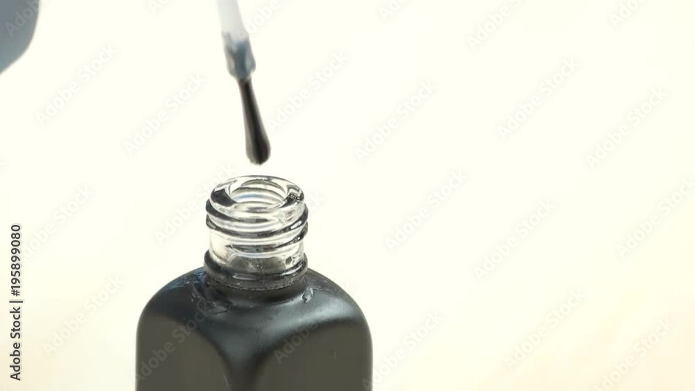 Transparent varnish dropping from brush, slow motion. Hand of nail beautician holding nail polish applicator with clear dropping varnish close up. Transparent varnish dropping from brush, slow motion. Hand of nail beautician holding nail polish applicator with clear dropping varnish close up.