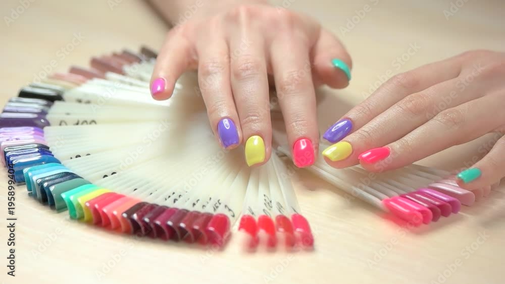 Slow motion hands choosing nail color. Beautiful female hands with pastel manicure and nail color palette on table in nail salon. Slow motion hands choosing nail color. Beautiful female hands with pastel manicure and nail color palette on table in nail salon.