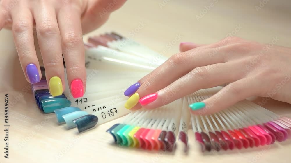 Slow motion hands choosing nail color. Close up young woman well-groomed hands with perfect summer manicure and nail color palette. Choice of nail color in beauty salon. Slow motion hands choosing nail color. Close up young woman well-groomed hands with perfect summer manicure and nail color palette. Choice of nail color in beauty salon.