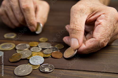 Hands of beggar with few coins. The concept of poverty . An elderly person on pension holds coins on wooden table background